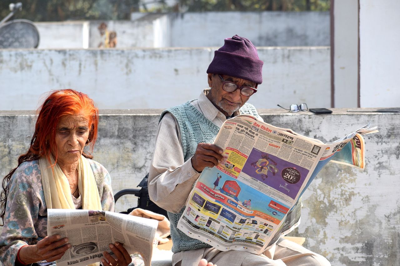 An elderly couple enjoys reading newspapers outside on a sunny day, reflecting a peaceful moment.